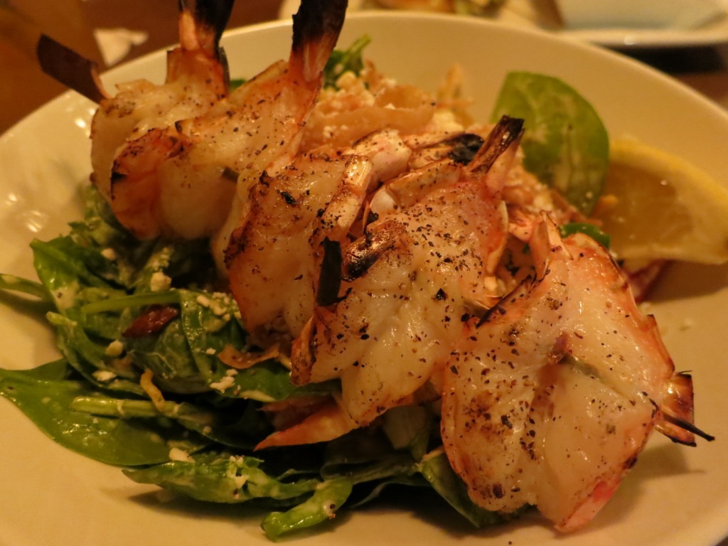 Spinach Salad with Grilled Shrimp Skewer of grilled shrimp, baby spinach, Mandarin oranges, red peppers, egg, bacon, crisp onion strings, Lo Mein noodles and feta cheese in an orange